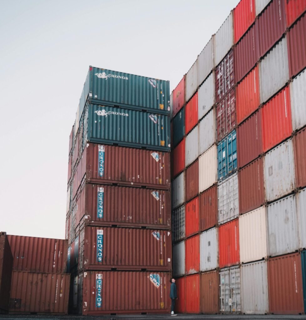 Stacks of colorful cargo containers at an industrial shipping yard, reflecting on wet ground.
